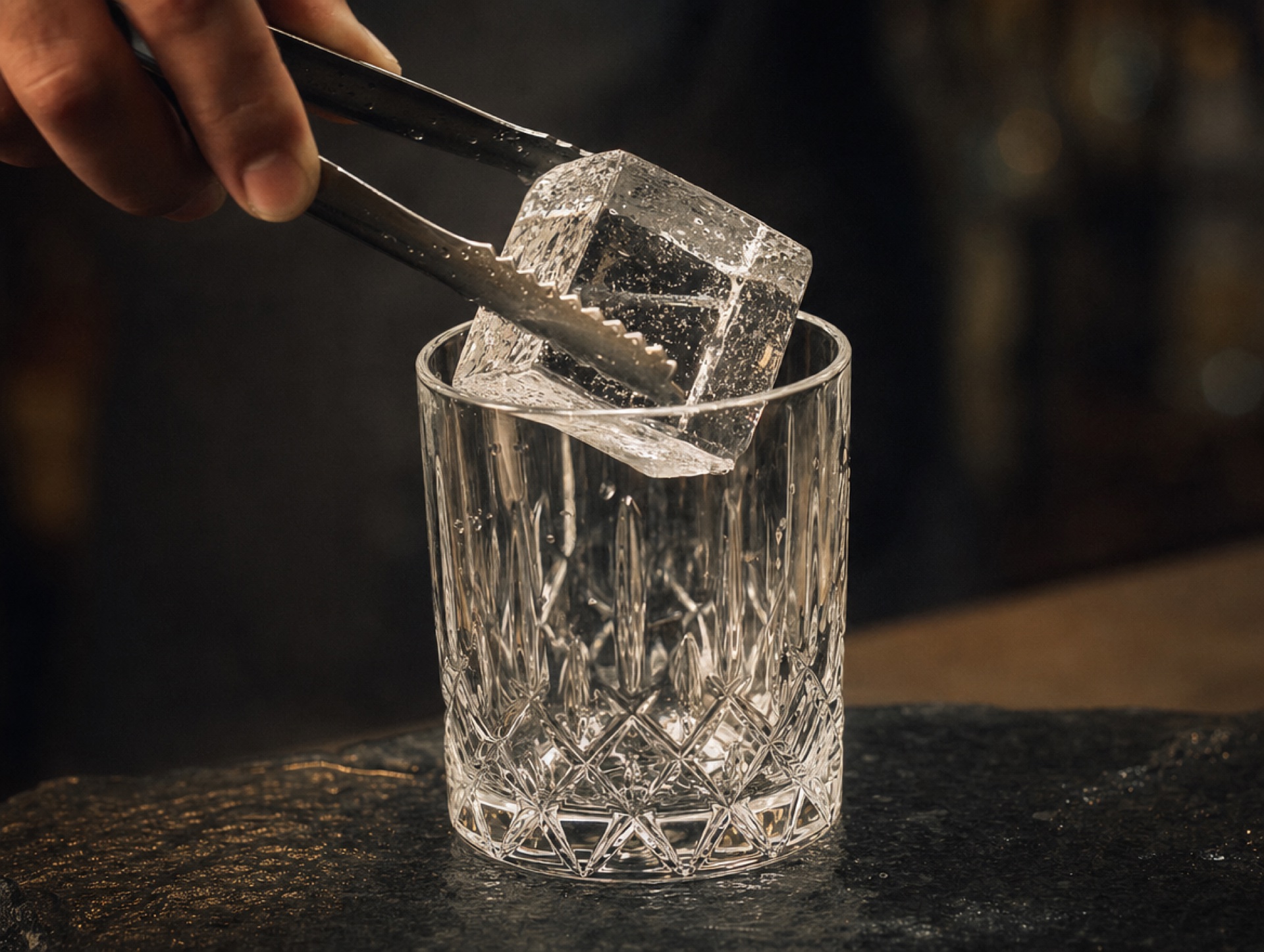 Hand-geschnitzter klarer Eiswürfel wird in ein Tumbler-Glas gelegt