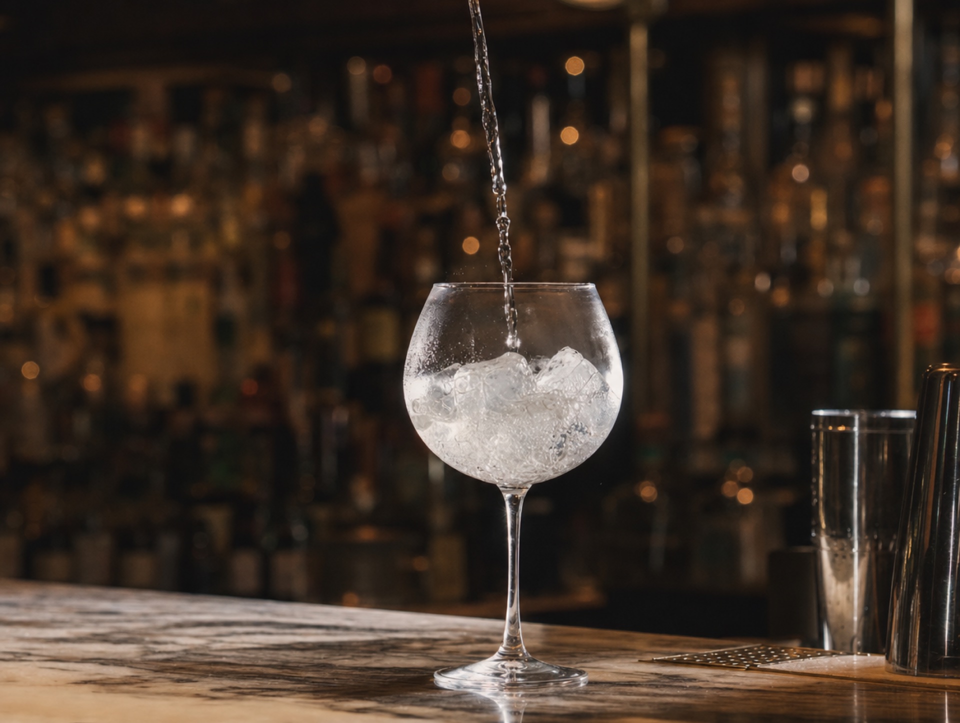 Hand eines Bartenders gießt Tonic aus der Höhe in ein Copa-Glas