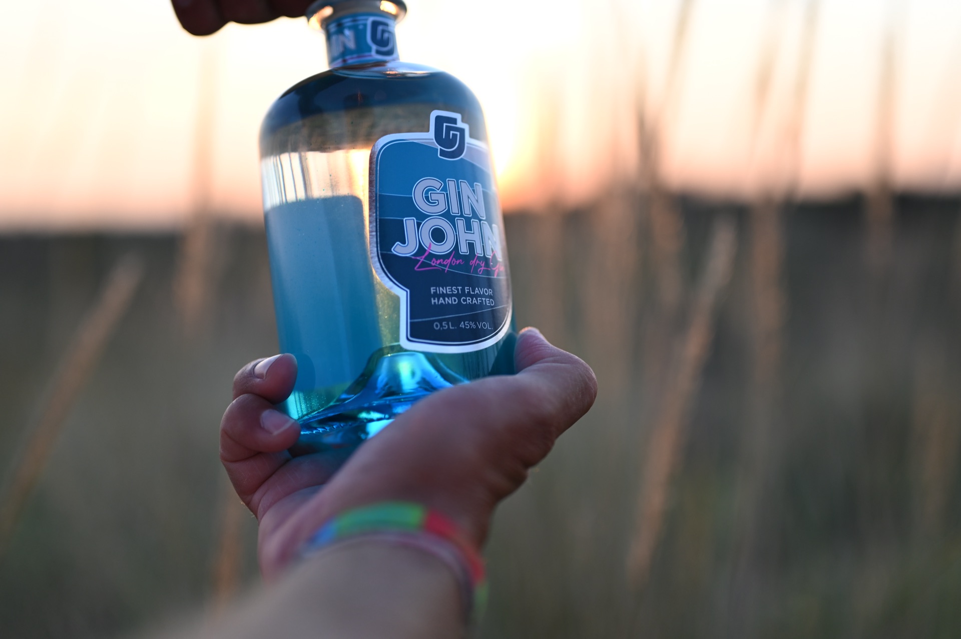 Gin John in der Hand bei Sonnenuntergang im Gras