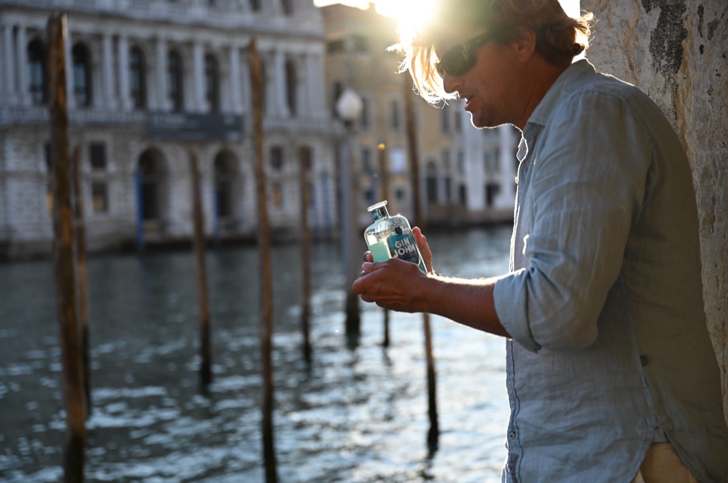Mann lehnt an alter Mauer am Canal Grande mit Gin John in der Hand