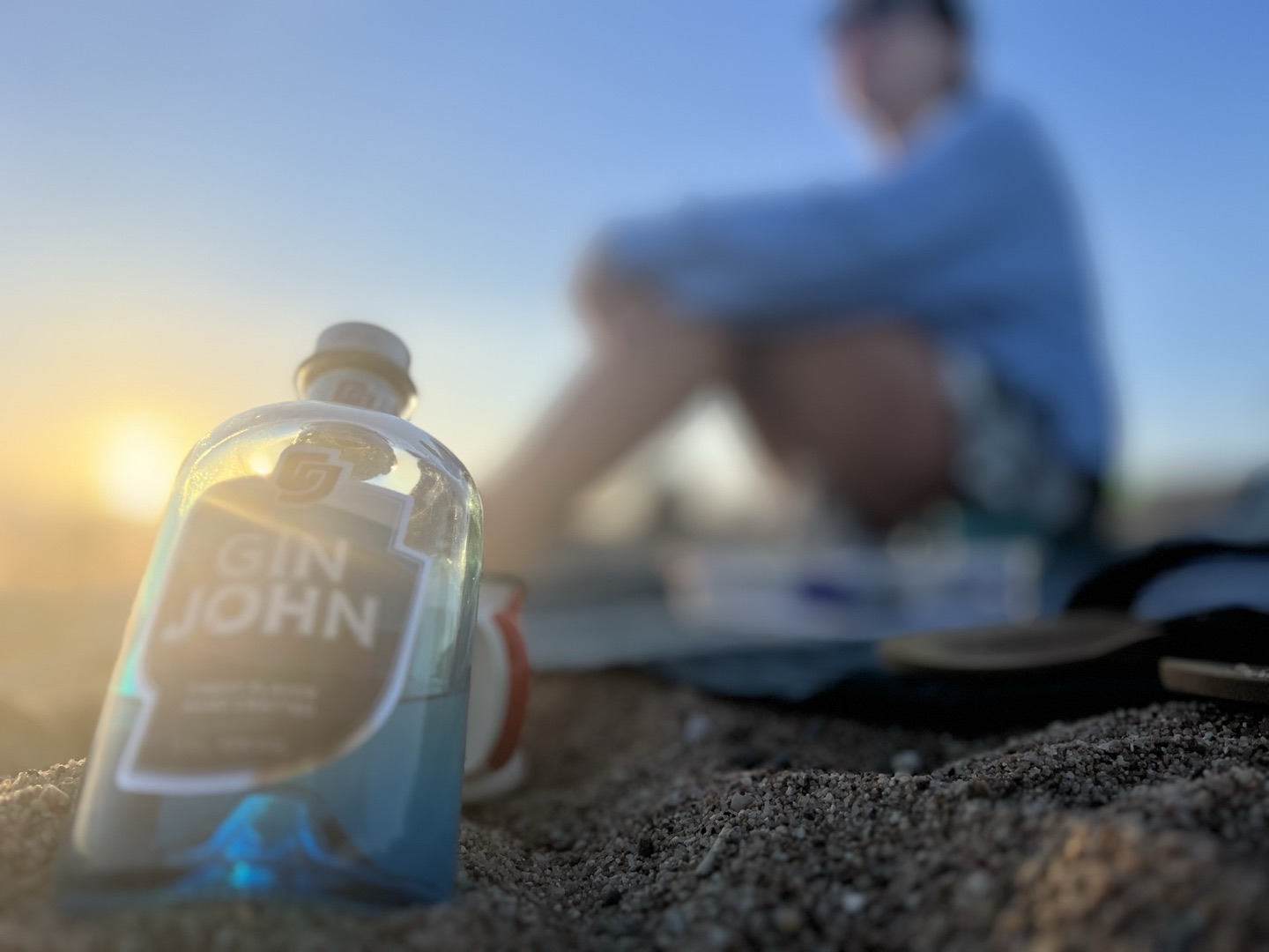 Gin John im Sand bei Sonnenuntergang mit Person im Hintergrund
